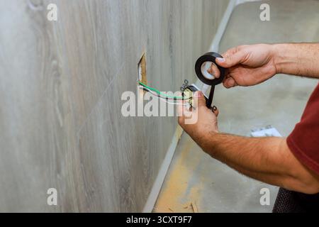 Elektriker wickelt elektrische Leitungen mit Klebeband, während bei der Renovierung von Häusern an der Verkabelung gearbeitet wird. Stockfoto