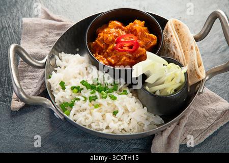 Heißes scharfes Hühnchen Tikka Masala in der Schüssel auf dunklem Hintergrund. Hühnercurry mit Reis, Brot und Kräutern. Traditionelles indisches Gericht. Draufsicht. Stockfoto