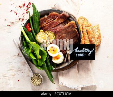 Gegrilltes Schweinefleisch mit grünem Salat und Gemüse auf Teller auf hellem Hintergrund. Draufsicht. Stockfoto