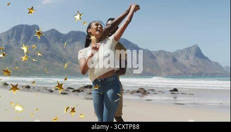 Tanzendes erwachsenes Paar, das sich am Sandstrand dreht, mit dekorativen goldenen Sternen Stockfoto