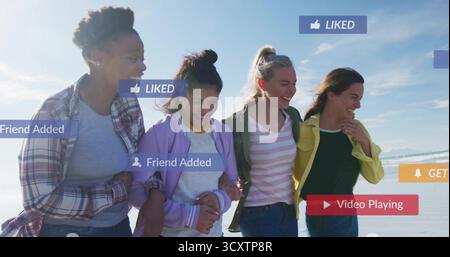Vier Freunde schlendern Arm in Arm am Sandstrand, mit beliebten Spielsymbolen, die von Freunden hinzugefügt wurden Stockfoto
