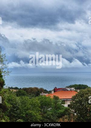 Stürmischer Himmel über dem Meer. Himmel vor Regen. Düsterer Himmel über dem Hügel und den Häusern und dem Meer Stockfoto
