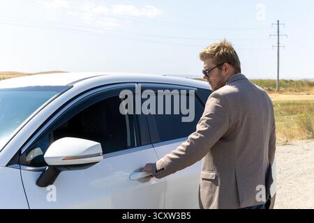 Ein Mann greift, um die Tür eines weißen Autos zu öffnen Stockfoto