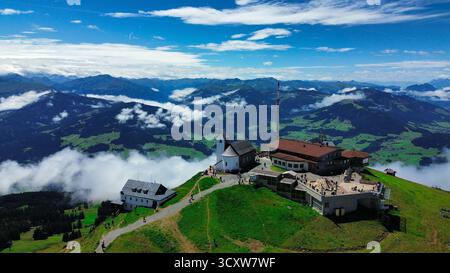 Malerische Berglandschaft mit einer Kapelle und Seilbahnstation über den Wolken, von einer Drohne erfasst. Ein atemberaubendes Alpenpanorama mit grünem Hang Stockfoto