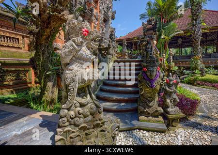 Aufwändig geschnitzte Steinstatuen, die mit Blumen verziert sind, am Puri Langon Tempel in Ubud, Gianyar, Bali, Indonesien. Stockfoto