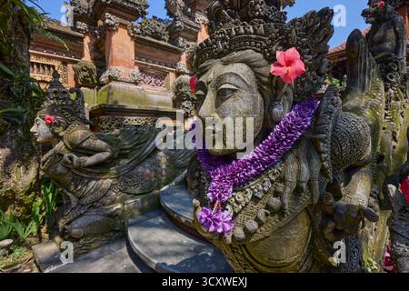 Aufwändig geschnitzte Steinstatuen, die mit Blumen verziert sind, am Puri Langon Tempel in Ubud, Gianyar, Bali, Indonesien. Stockfoto