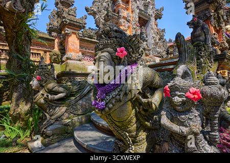 Aufwändig geschnitzte Steinstatuen, die mit Blumen verziert sind, am Puri Langon Tempel in Ubud, Gianyar, Bali, Indonesien. Stockfoto