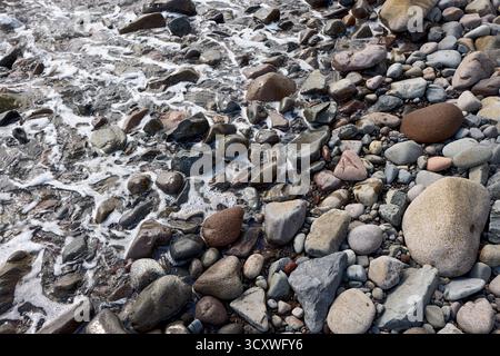 Nahaufnahme der Meeresbrandung, die die Küstenkiesel am Strand in der Nähe von Amed, Karangasem Regency, Bali, Indonesien berührt. Stockfoto
