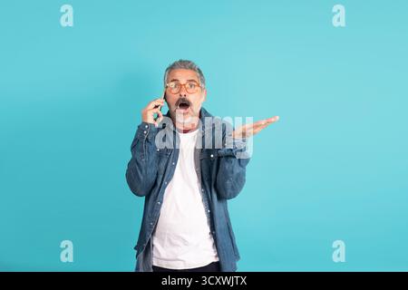 Ein reifer Mann reagiert überraschend und öffnet den Mund während eines Telefongesprächs Stockfoto