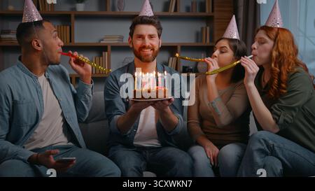 Vier multirassische fröhliche Freunde auf der Heimfeier gratulieren Geburtstagsmann lachen sorglos lächelnd halten Kuchen mit Kerzen glückliche Gruppen Männer Stockfoto