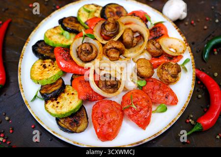 Gegrilltes Gemüse: Rote und gelbe Paprika, Zucchini, Auberginen, Pilze, Tomaten und Zwiebeln serviert auf rustikalem Holzschneidebrett, weißer Tischhintergrund, Blick von oben. Hochwertige Fotos Stockfoto