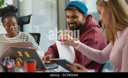 Glückliches Lächeln positives Diversity-Business-Team im informellen Startup-Büro spricht freundlich sorglos arbeiten in Laptop zeigen mit Computer diskutieren Stockfoto