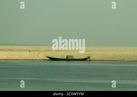 Ein traditionelles hölzernes Fischerboot liegt neben einem riesigen, einsamen Sandsaibling unter einem hellen Himmel. Unfruchtbarer Sand, der auf das ruhige, türkisfarbene Wasser der r Stockfoto