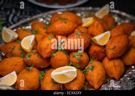 Traditionelle türkische und Arap Icli Kofte serviert mit Zitronenscheiben auf Silbertablett. Goldene gebratene Bulgur-Fleischbällchen Kibbeh. Beliebtes Gericht Stockfoto