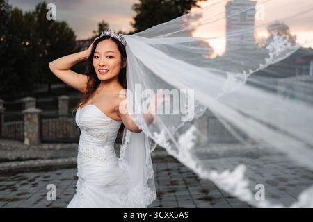 Chinesische Braut lächelt mit Hochzeitsschleier, der im Wind weht Stockfoto