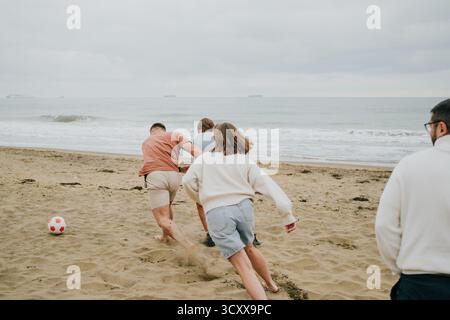Eine Gruppe von Leuten spielt ein Spiel Beach Frisbee. Der Mann im rosa Hemd versucht, die Frau im weißen Hemd davon abzuhalten, die Fritten zu fangen Stockfoto