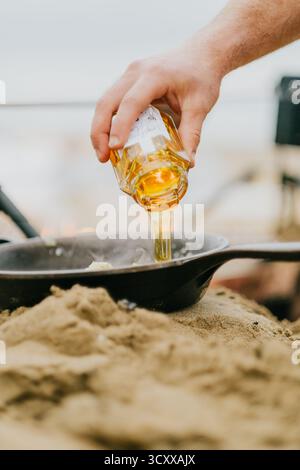 Eine Person, die Honig in eine Pfanne gießt. Der Honig ist Golden und die Pfanne schwarz. Die Szene spielt an einem Sandstrand Stockfoto