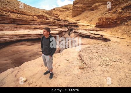 Trockenes Flussbett, Wildnis. Natürliche Wüstenlandschaft. Sandsteinstruktur. Junger Mann, der im Red Canyon in der Negev-Wüste in der Nähe von Eilat, Israel, spaziert. Stockfoto