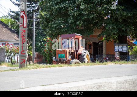 Ein alter roter IMT-Traktor, der an einem sonnigen Sommertag unter einem Baum im Dorf Vrdnik, Vojvodina, Serbien, geparkt wurde Stockfoto