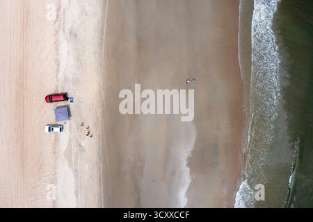 Aus der Vogelperspektive von oben nach unten von Geländefahrzeugen am Strand in der Nähe des Ozeans mit einem Zelt auf dem Sand Stockfoto