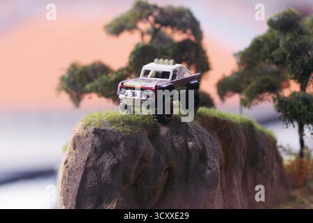Ein Geländewagen in weiß mit roten und schwarzen Akzenten steht dramatisch am Rand einer felsigen Klippe in einem detaillierten Diorama Stockfoto