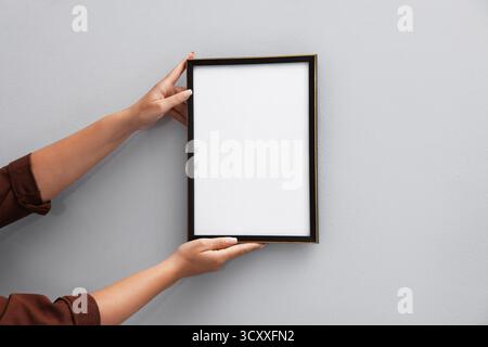Frau, die einen leeren Diplom-Rahmen an einer Lichtwand hängt, Großaufnahme. Modell für Design Stockfoto