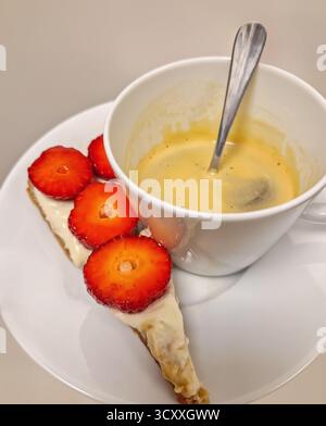 Eine Tasse Espresso mit Crema auf einer Untertasse mit einer Scheibe Torte, garniert mit cremig weißen Erdbeeren, für einen appetitlichen Shot o Stockfoto