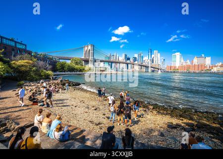 New York City, USA, 16. September 2024: New York City East River Pebble Beach in Brooklyn View. Die Leute genießen die Aussicht auf die Skyline von Manhattan. Stockfoto