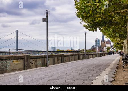 Leere, von Bäumen gesäumte Promenade entlang des Rheins mit weit entferntem Kirchturm und urbaner Skyline im bewölkten Herbst Düsseldorf Deutschland Stockfoto