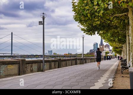 Joggen auf der von Bäumen gesäumten Rheinpromenade mit historischem Uhrenturm und City Skyline im Herbst Düsseldorf Deutschland Stockfoto