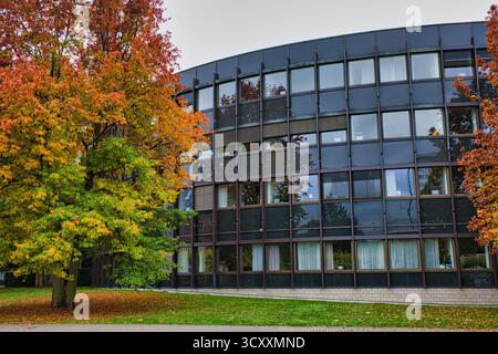 Moderne geschwungene Bürogebäude-Fassade umgeben von lebhaften Herbstahornbäumen auf Grasrasen im Herbst Düsseldorf Deutschland Stockfoto