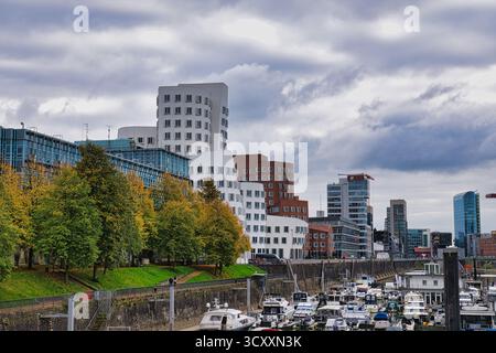 Gehry entwarf Twisted Buildings mit Blick auf den geschäftigen Yachthafen mit angedockten Booten und Herbstbäumen in Düsseldorf Deutschland Stockfoto