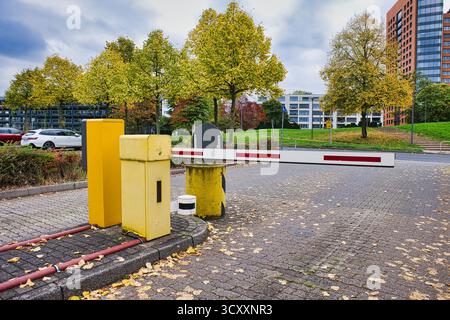 Gelbes Parksperrtor mit rotem und weißem Arm am Eingang zum gepflasterten Grundstück, umgeben von herbstlichen gelben Bäumen und modernen Gebäuden im Hintergrund Stockfoto