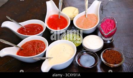 Verschiedene Saucen in weißen Schüsseln, die einen Kreis auf einem Holztisch mit Gewürzen, einer Serviette und einer Nudelnadel bilden. Hochwertige Fotos Stockfoto