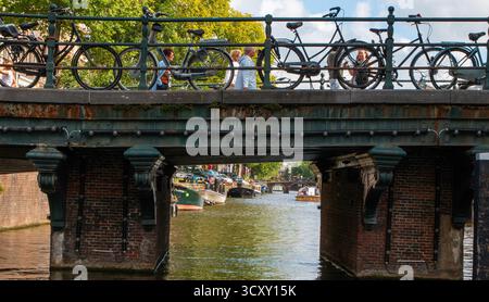 Amsterdam, Niederlande - 5. August 2025: Die Menschen schlendern auf einer Brücke, während die Fahrräder über einem friedlichen Kanal in Amsterdam ruhen. Stockfoto
