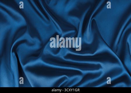 Zerknitterte, zerknitterte, blau gefärbte, glänzende Seidensatin-Textur. Glänzender glatter Stoff mit weichen Falten, Stoff mit Wellenvorhang. Eleganter und satter Hintergrund, Stockfoto