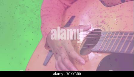 Eine Frau in rosa gepunktetem Hemd im Studio, mit Akustikgitarre und grünem Chroma-Key-Hintergrund Stockfoto