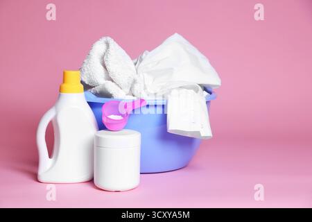 Plastikbecken mit Wäsche und Waschmitteln auf rosafarbenem Hintergrund. Leerzeichen für Text Stockfoto