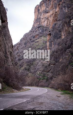 Eine kurvige Straße, die durch einen engen Canyon führt, flankiert von steilen, zerklüfteten Klippen auf beiden Seiten. Stockfoto