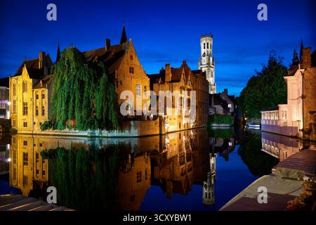 Historische Brügge Rozenhoedkaai Nachtbesprechung. Abenddämmerung auf dem historischen Rozenhoedkaai von Brügge, Belgien, mit mittelalterlichen Gebäuden, Kanal und Glockenturm. Stockfoto