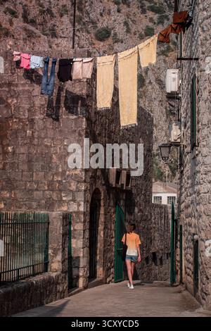 Frisch gewaschene Kleidung trocknet auf einem Wäscheleinen in der Sonne. Eine enge Straße in der Altstadt, wo ein Mädchen schlendert. Stockfoto