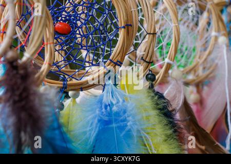 Nahaufnahme farbenfroher Traumfänger mit blauen und gelben Federn, Holzperlen und gewebten Fäden, die traditionelle Handwerkskunst repräsentieren, c Stockfoto