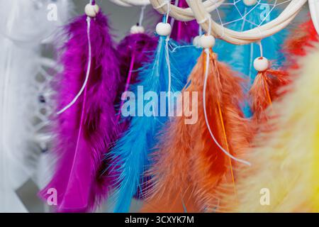 Nahaufnahme farbenfroher Traumfänger-Federn in violetten, blauen, orangen und gelben Tönen, die zart mit Holzperlen hängen – ein handgefertigtes Bohemian d Stockfoto
