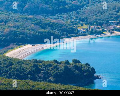 Ein Blick aus der Vogelperspektive auf den ruhigen Strand von Avlaki auf Korfu, Griechenland, mit klarem türkisfarbenem Wasser und üppigen grünen Hügeln an einem sonnigen Tag Stockfoto