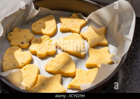 Ein Backblech gefüllt mit ungekochten, geformten Keksen, die für das Backen im Ofen bereit sind, der Prozess des selbstgebackenen Backens und eine Vielzahl von festlichen Ausstechern. Stockfoto