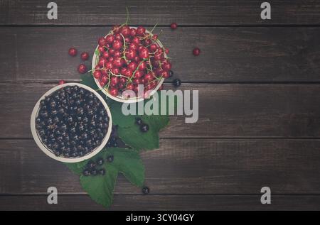 Schwarze und rote Johannisbeeren in Schüsseln, Hintergrund mit Blick von oben auf rustikalem Holz Stockfoto