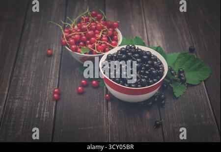 Schwarze und rote Johannisbeeren in Schüsseln Nahaufnahme Hintergrund auf rustikalem Holz Stockfoto