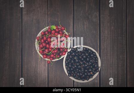 Schwarze und rote Johannisbeeren in Schüsseln, Hintergrund mit Blick von oben auf rustikalem Holz Stockfoto