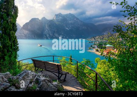 Panoramablick von einer Bank mit Blick auf Torbole sul Garda und das türkisfarbene Wasser des oberen Gardasees (Alto Garda). Berg und eine Kreuzfahrt Boa Stockfoto