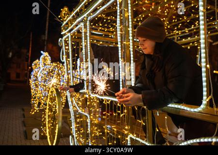 Die Weihnachtslichter der jungen Frau leuchten nachts in der festlichen beleuchteten Kutschenstruktur während der Feiertage Stockfoto